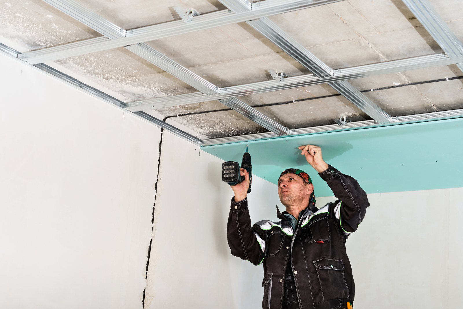 Construction worker assembly suspended ceiling with drywall and fixing the drywall to the ceiling metal frame with screwdriver.